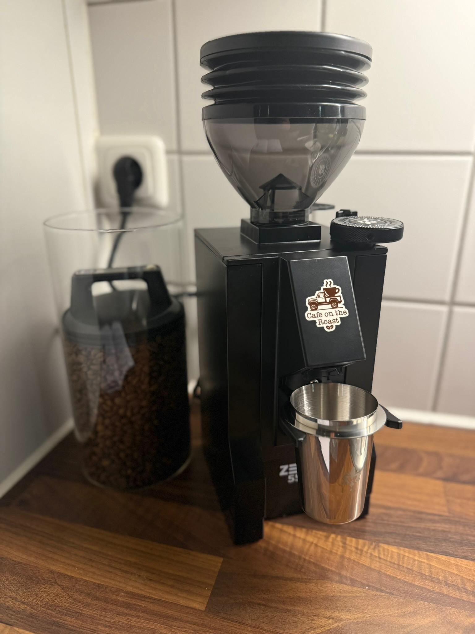 CotR branded grinder with logo sticker on warm wood surface, coffee beans in hopper